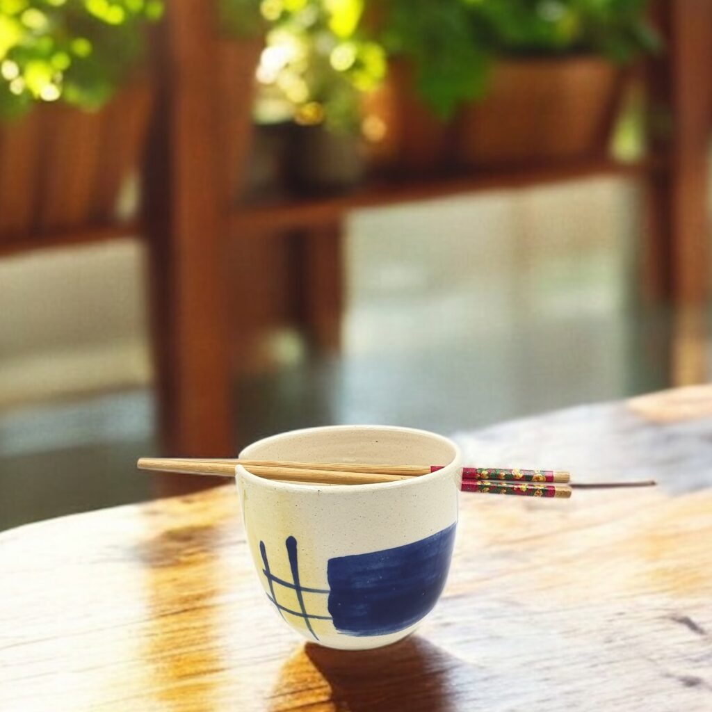 Leafbud Whispers ramen bowl with chopsticks on a sunlit wooden table, surrounded by plants