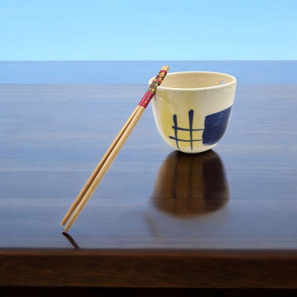 Handmade Leafbud ramen bowl on a dark wooden table by the sea, chopsticks leaning against it